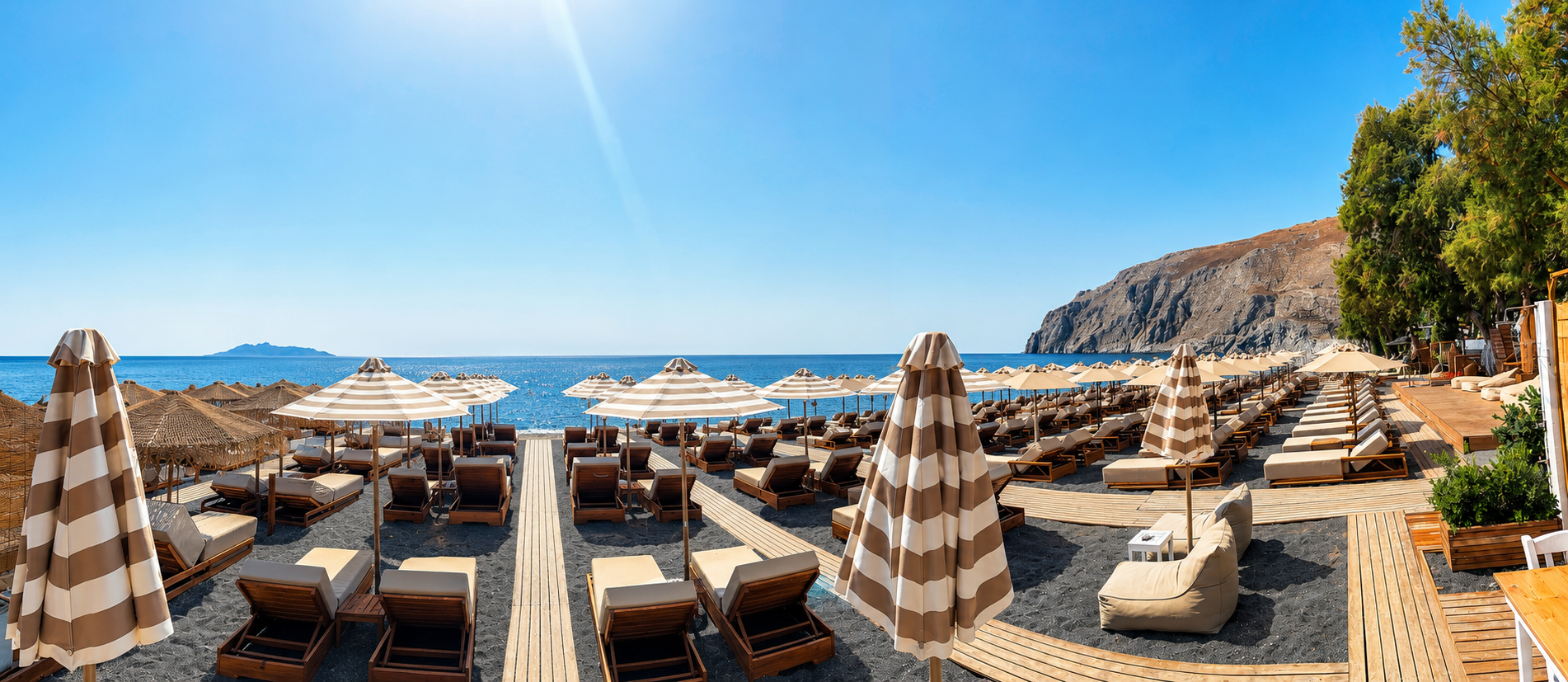 Ariale Beach con ombrelloni a strisce, lettini e vista sul mare di Kamari
